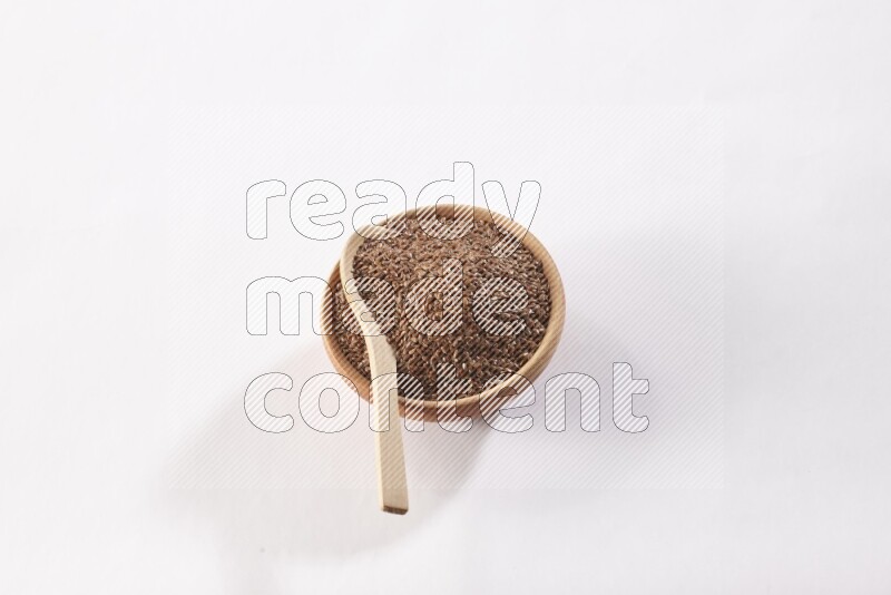 A wooden bowl full of flax seeds and a wooden spoon full of flax seeds in it on a white flooring