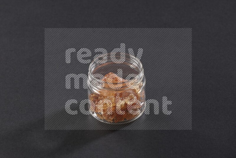 A glass jar full of gum arabic on black flooring
