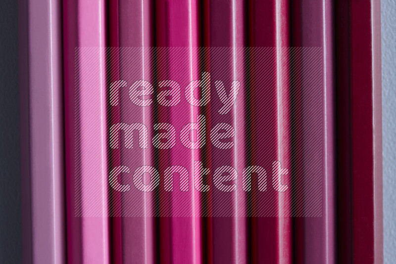 A collection of sharpened colored pencils arranged showcasing a gradient of pink hues on grey background