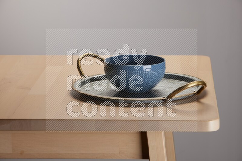 blue bowl placed on a rounded stainless steel metal tray with golden handels on the edge of wooden table