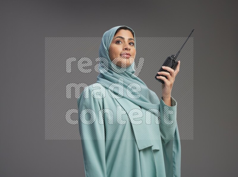 Saudi Woman wearing Abaya standing holding walkie-talkie on Gray background