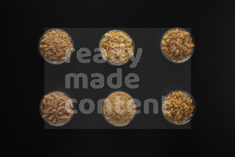 Different pasta types in 6 glass bowls on black background
