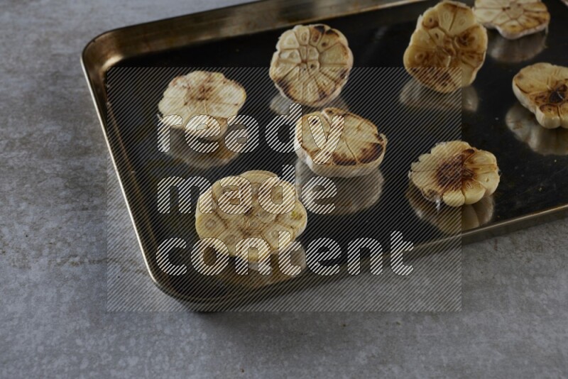 half's roasted garlic in a stainless tray on a grey textured countertop
