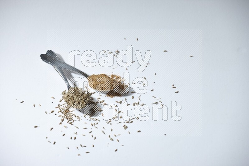 2 metal spoons full of cumin seeds and powder on white flooring