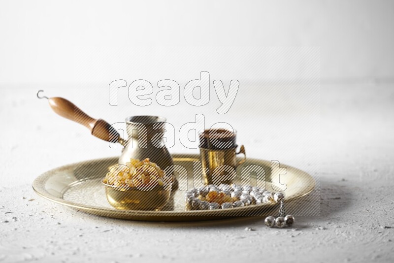 Raisins in a metal bowl with coffee and prayer beads on a tray in a light setup