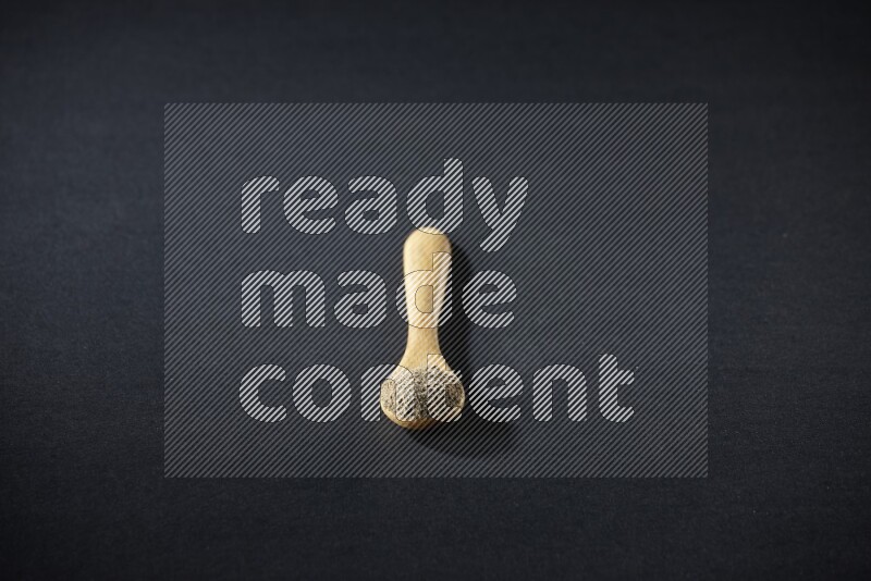 A wooden spoon full of cardamom powder on black flooring