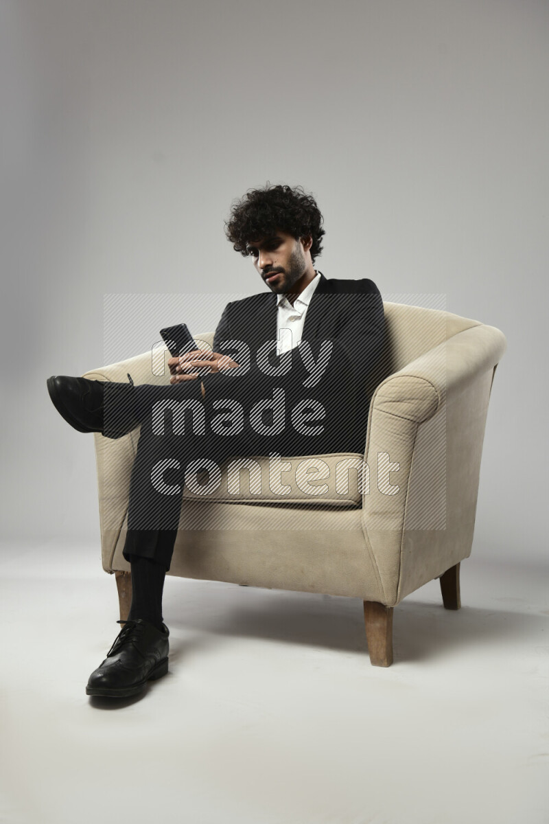 A man wearing formal sitting on a chair texting on the phone on white background