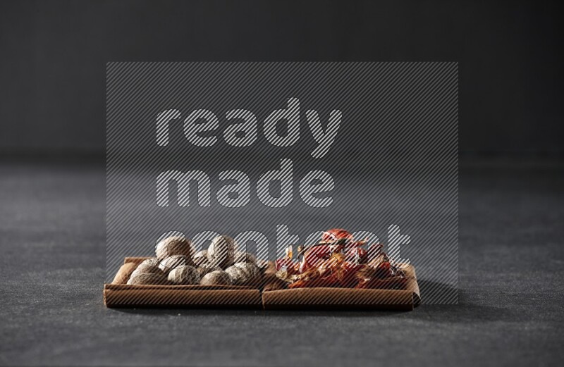 مربعان من أعواد القرفة ممتلئان بجوزة الطيب والفلفل الحار المجفف علي خلفية سوداء