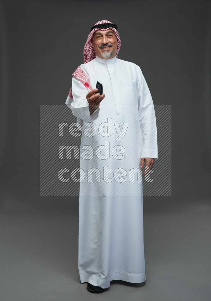 Saudi man with shomag Standing holding car key on gray background