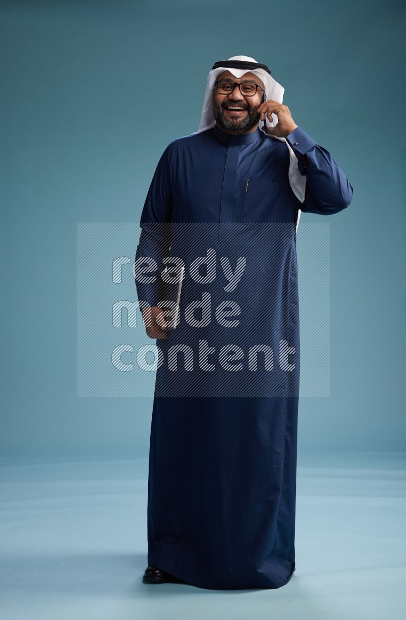 Saudi Man with shimag Standing talking on phone on blue background