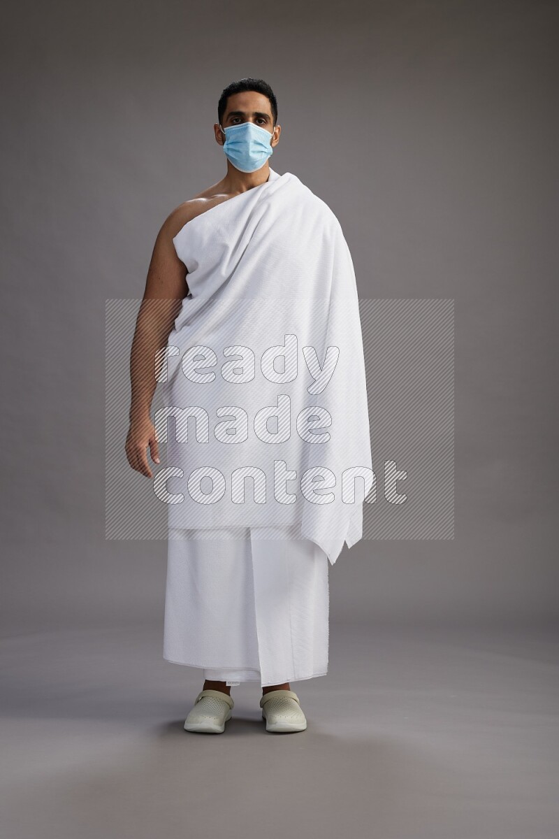 A man wearing Ehram with face mask Standing Interacting with the camera on gray background