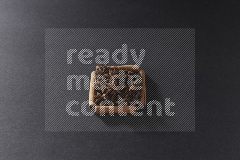 A single square of cinnamon sticks full of star anise on black flooring