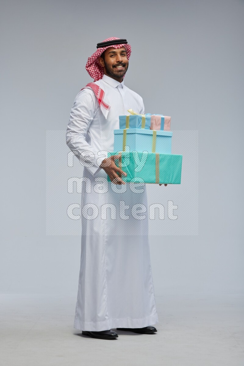 Saudi man Wearing Thob and shomag standing holding gift box on Gray background