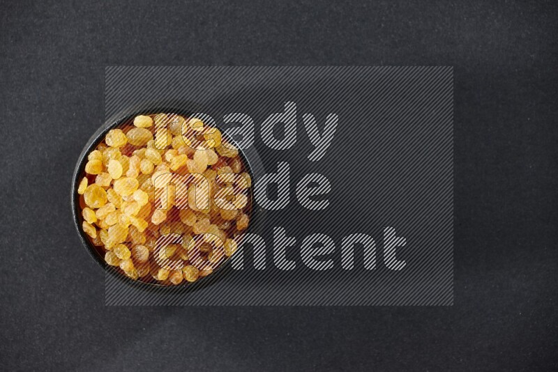 وعاء فخاري أسود ممتلئ بالزبيب الأصفر على خلفية سوداء