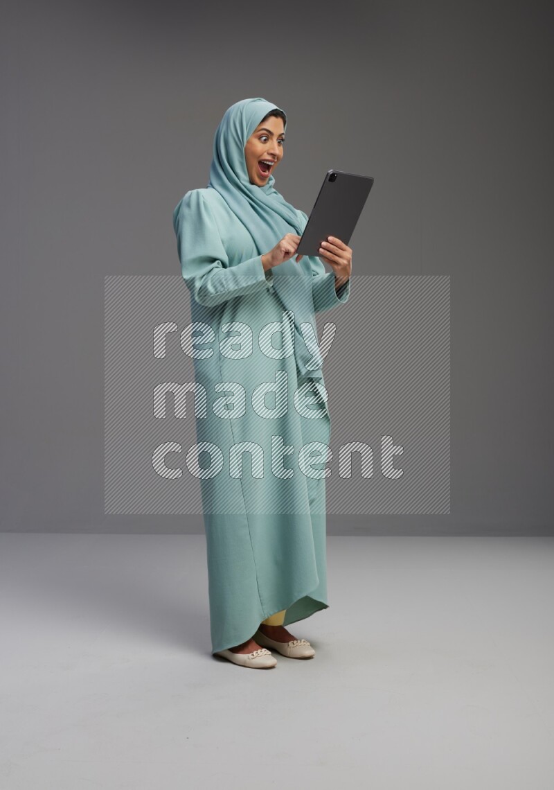 Saudi Woman wearing Abaya standing working on tablet on Gray background