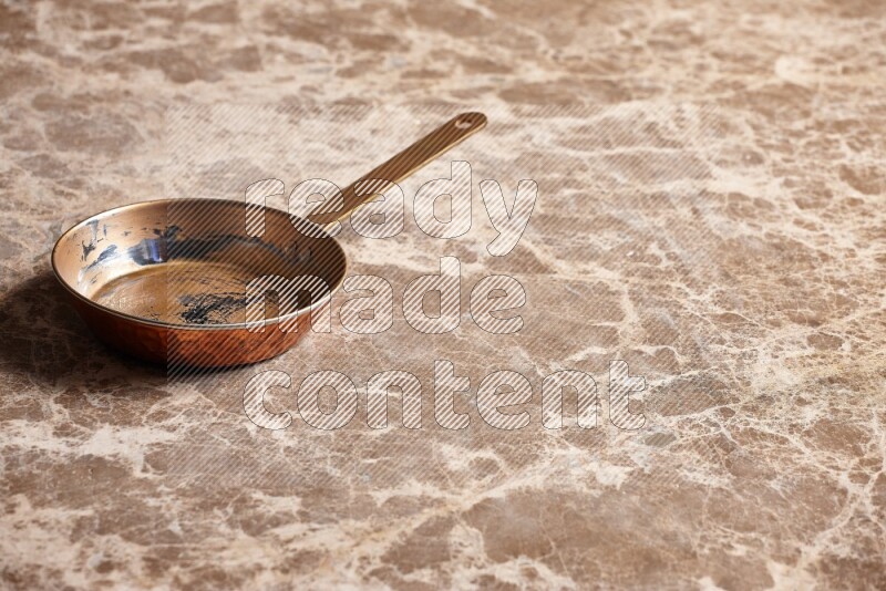 A small copper pan on beige marble background