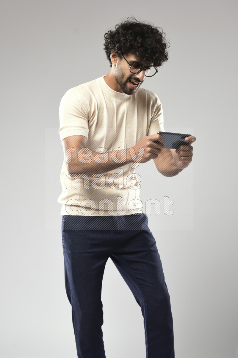 A man wearing casual standing and gaming on the phone on white background
