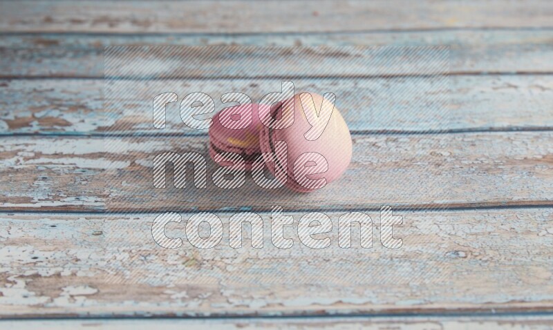 45º Shot of two Purple Strawberry macarons on light blue wooden background