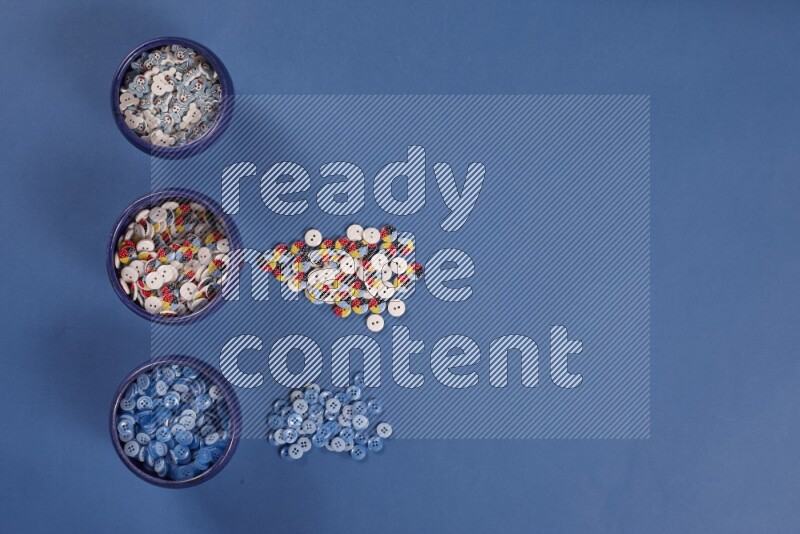 Multicolored pottery bowls full of colored buttons on blue background