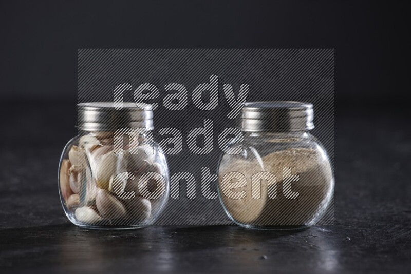 2 glass spice jars full of garlic powder and cloves on a textured black flooring