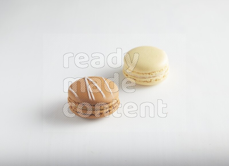45º Shot of of two assorted Brown Irish Cream, and Yellow Vanilla macarons on white background
