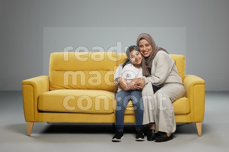 A girl with her mother sitting and interacting with the camera on gray background
