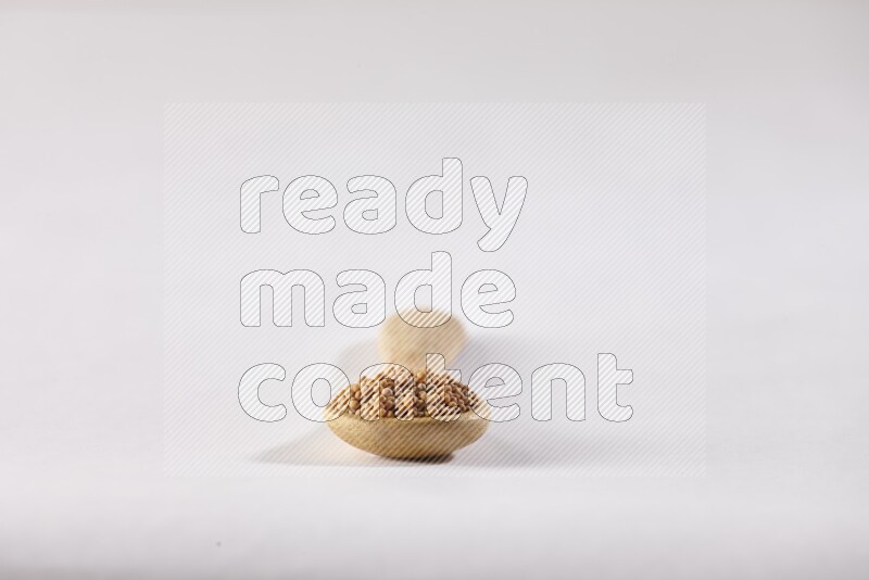 A wooden spoon full of mustard seeds on a white flooring