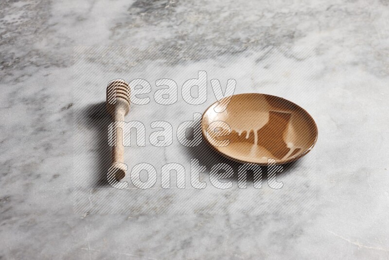 Multicolored pottery plate with wooden honey dipper on the side on grey marble background