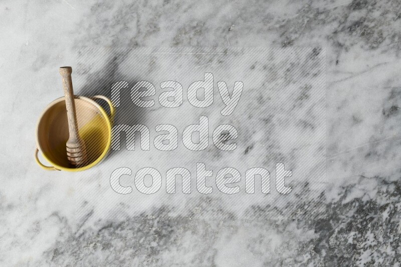 وعاء فخاري متعدد الألوان مع ملعقة عسل خشبية بداخله على خلفية من الرخام الرمادي