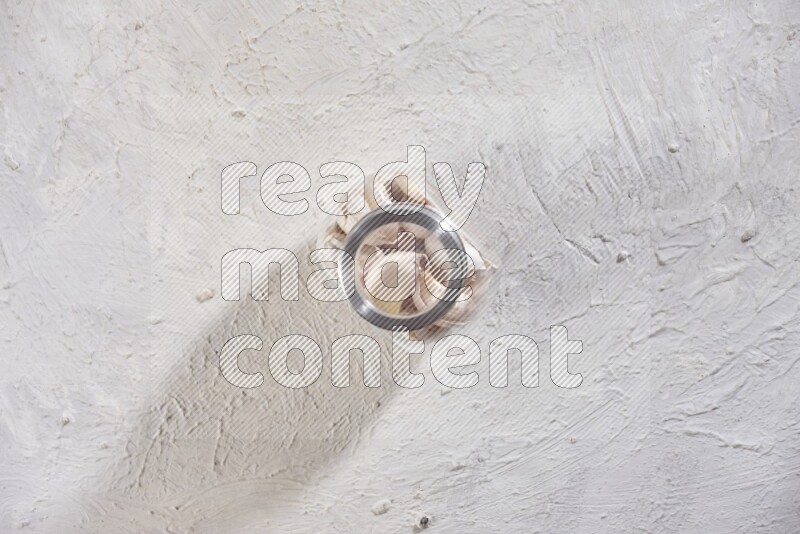 A glass spice jar full of garlic cloves on a textured white flooring