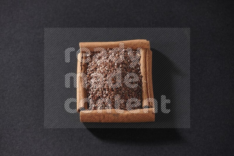 A single square of cinnamon sticks full of flaxseeds on black flooring