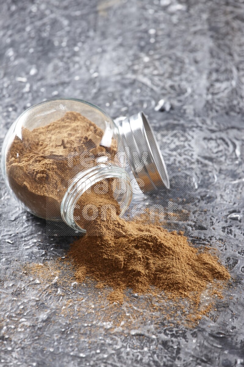 Flipped herbal glass jar full of cinnamon powder on textured black background