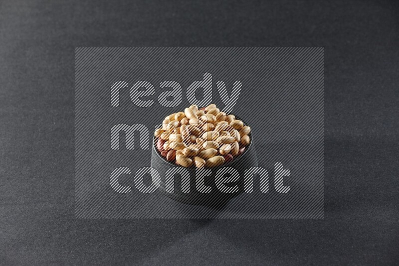 A black pottery bowl full of peeled peanuts on a black background in different angles