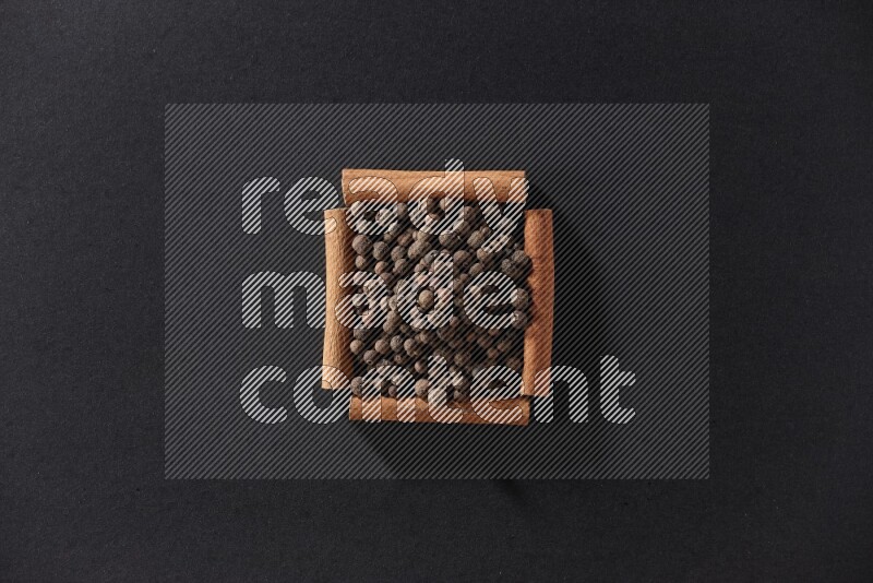 A single square of cinnamon sticks full of allspice on black flooring