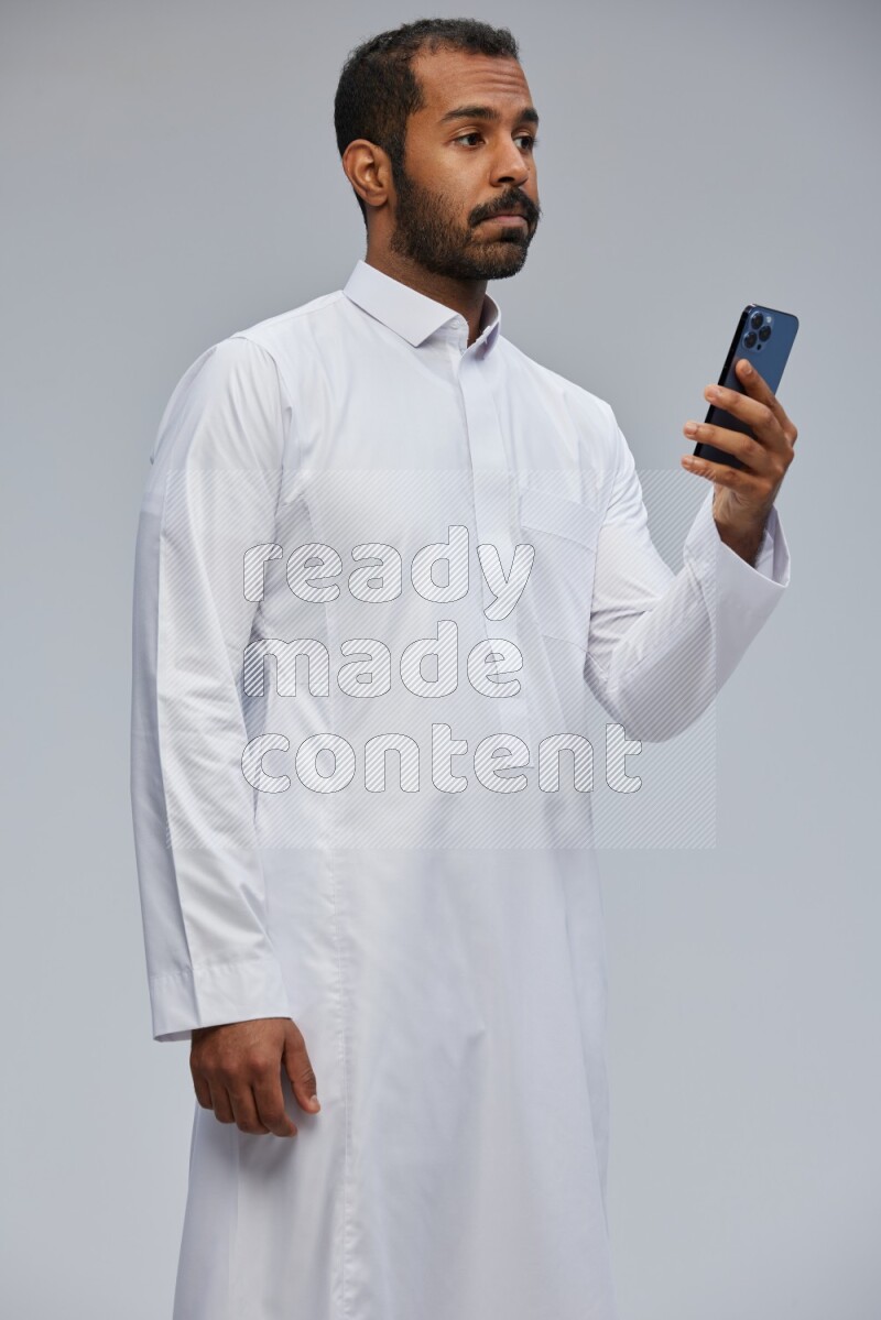 Saudi man wearing Thob standing texting on phone on Gray background