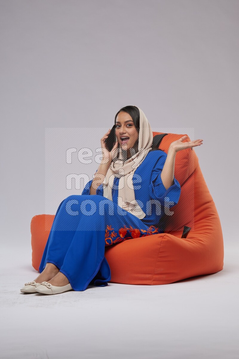 A Saudi woman wearing Jalabiya sitting on an orange beanbag and talking on the phone