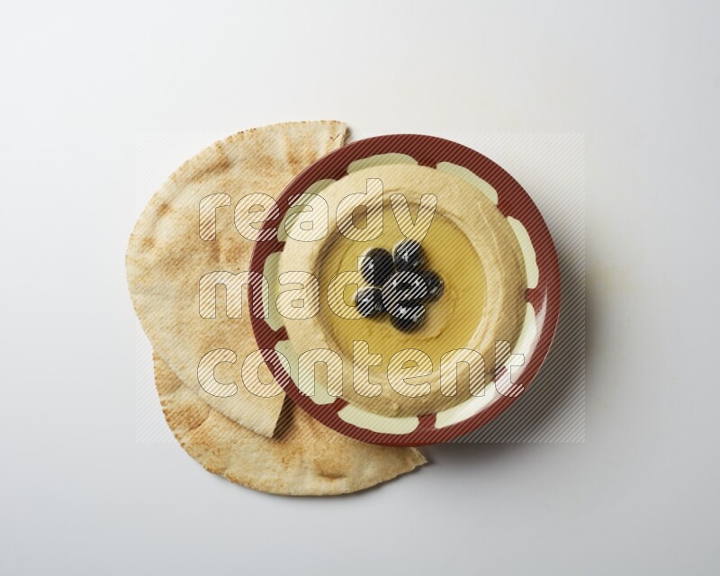 Hummus in a traditional plate garnished with black olives on a white background