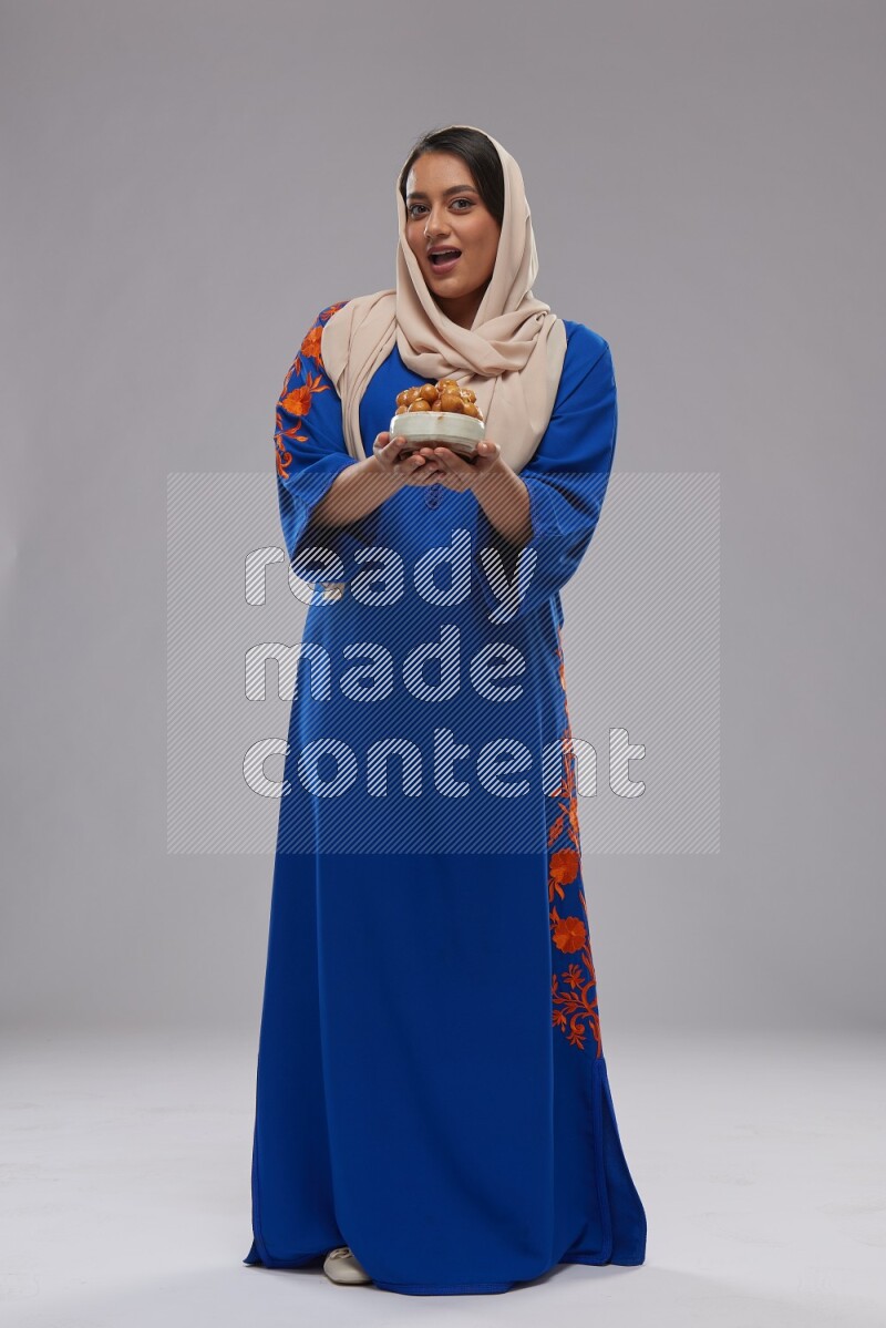 A Saudi woman standing wearing Jalabeya holding a plate of luqaimat