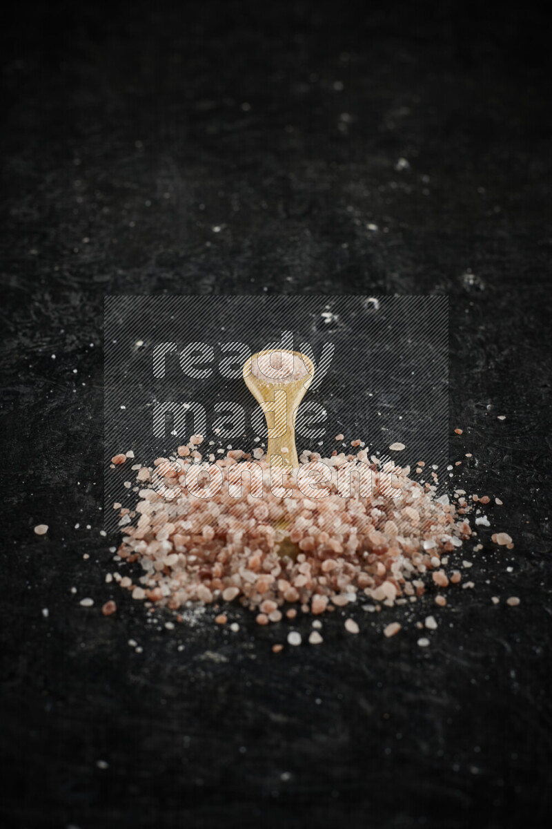 A wooden spoon full of pink himalayan salt on black background