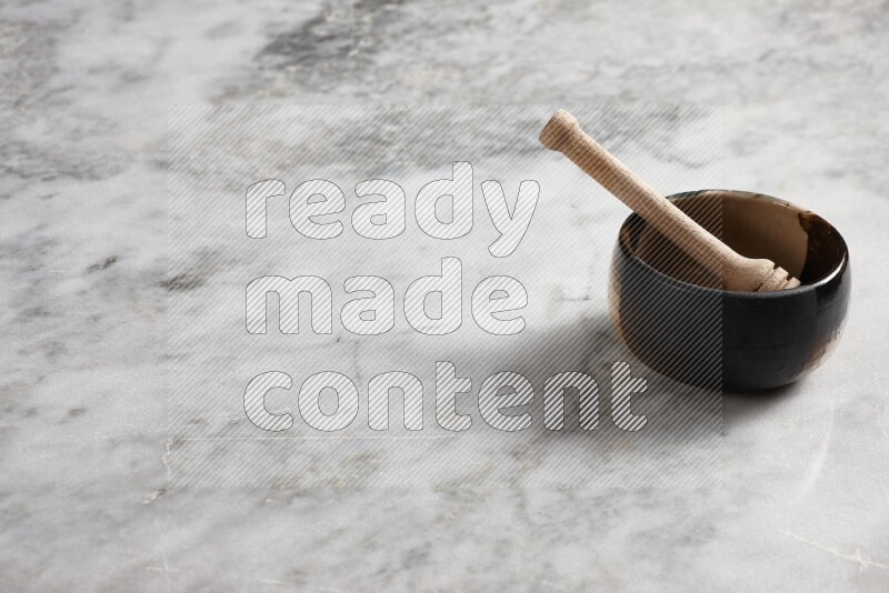 Multicolored pottery bowl with wooden honey dipper in it on grey marble background
