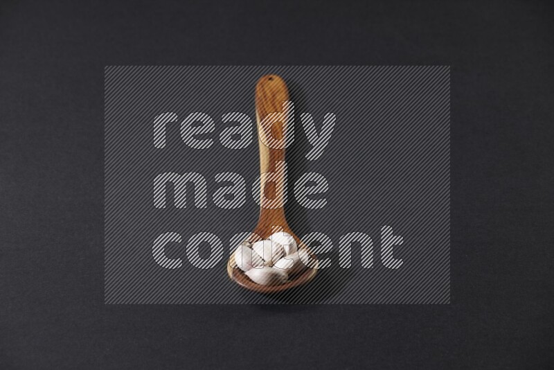 A wooden ladle full of garlic cloves on a black flooring