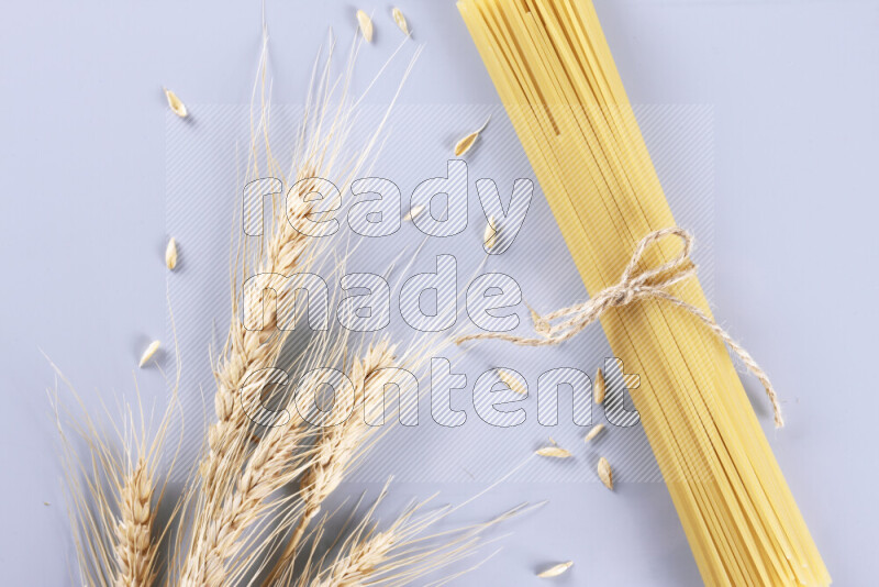 Raw pasta with wheat stalks on light blue background