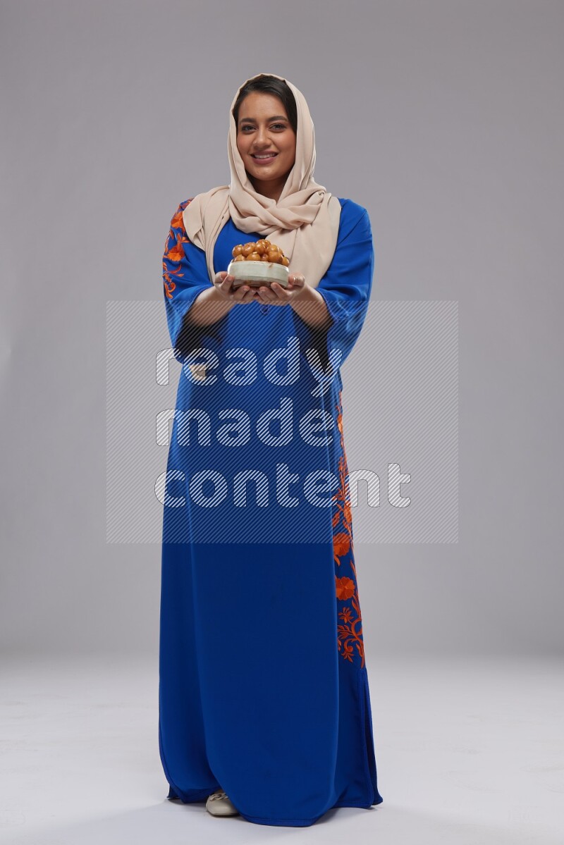 A Saudi woman standing wearing Jalabeya holding a plate of luqaimat