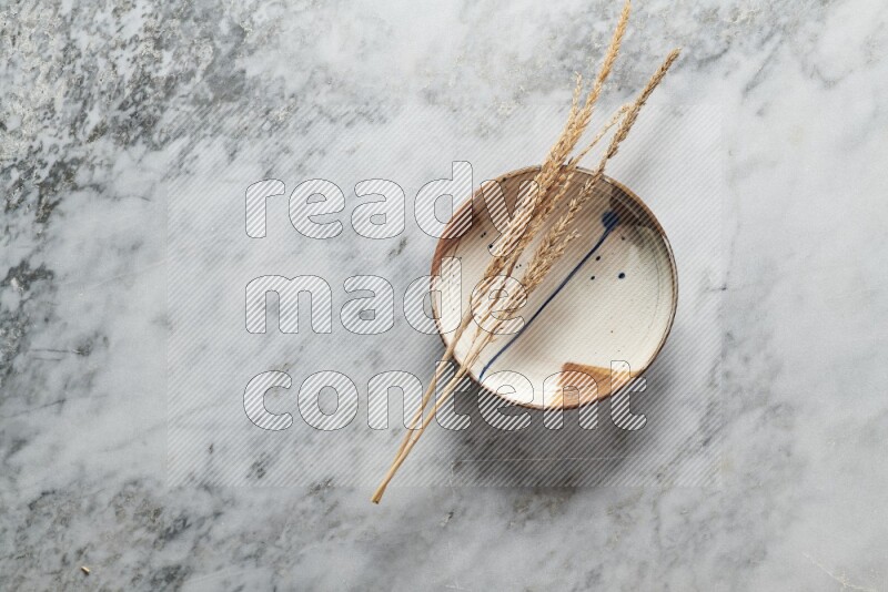 Wheat stalks on multicolored pottery plate on grey marble background