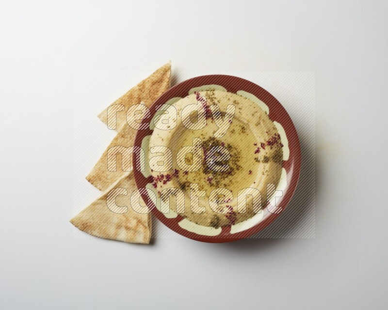 Hummus in a traditional plate garnished with zaatar & sumak on a white background