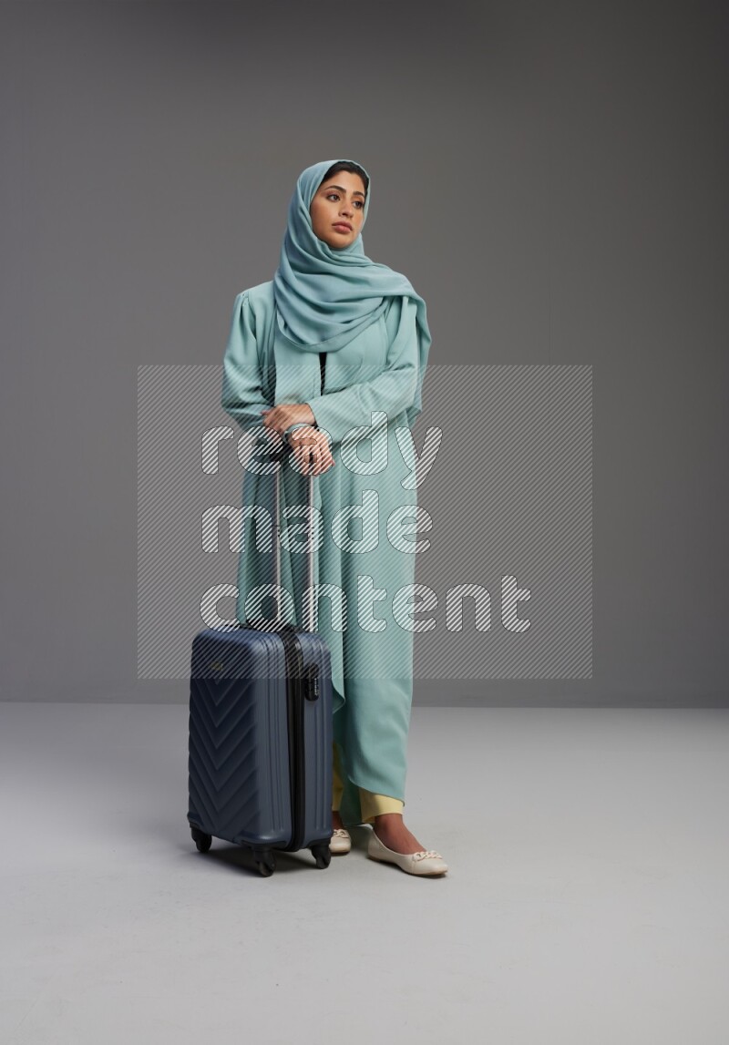 Saudi Woman wearing Abaya standing holding Travel bag on Gray background