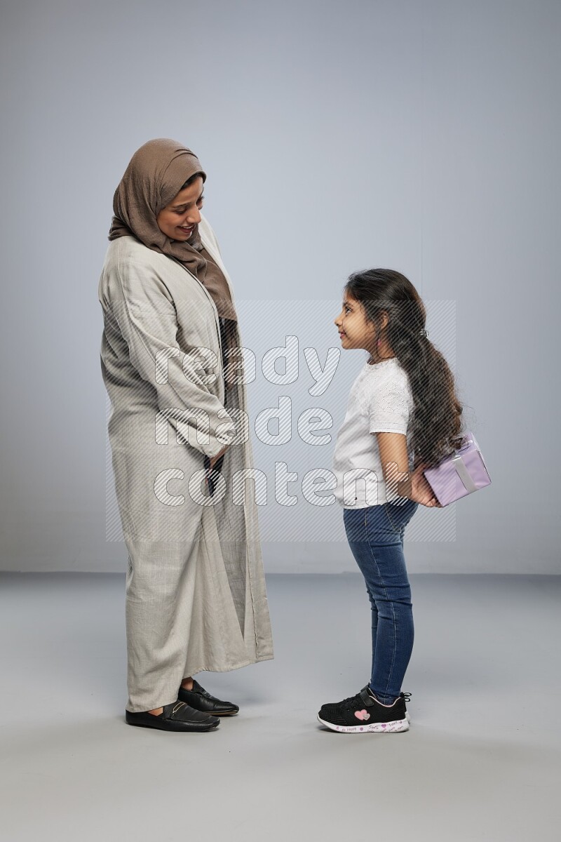 A girl standing hiding a gift behind her back for her mother on gray background
