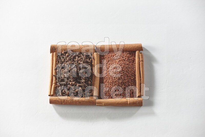 مربعان من أعواد القرفة ممتلئان بحب الرشاد والقرنفل علي خلفية بيضاء