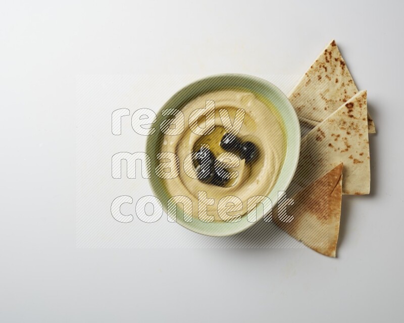 Hummus in a green plate garnished with black olives on a white background