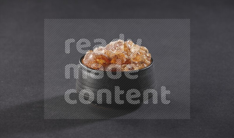 وعاء فخاري أسود ممتلئ بقطع الصمغ العربي علي خلفية سوداء